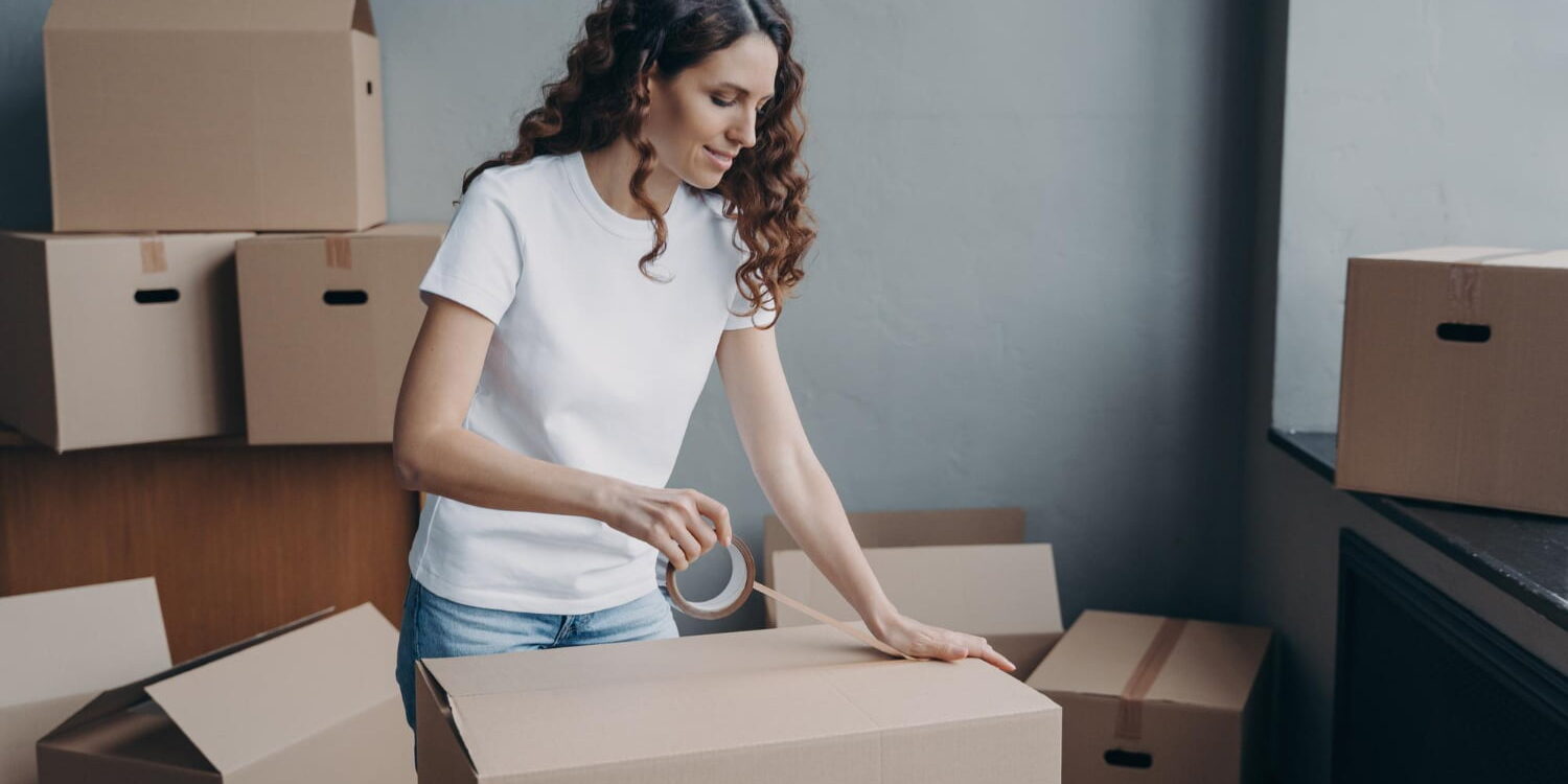 female-sealing-cardboard-box-parcel-with-adhesive-tape-moving-day-removal-service-relocation