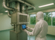A cleanroom technician in full protective suit operates a modern HVAC system inside a sterile room, with tropical palm trees visible through large windows — representing cleanroom HVAC tropical climates balancing energy, comfort, and filtration.