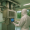 A cleanroom technician in full protective suit operates a modern HVAC system inside a sterile room, with tropical palm trees visible through large windows — representing cleanroom HVAC tropical climates balancing energy, comfort, and filtration.