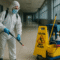 A janitorial worker in protective gear disinfecting an industrial corridor with professional cleaning tools and safety signage, illustrating the concept of industrial hygiene infection prevention through data-driven cleaning systems.