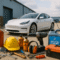 A wide-angle realistic photograph of automotive MRO tools, lubricants, safety gear, and equipment placed in front of a charging electric vehicle at a modern warehouse in Java. The scene symbolizes evolving Java automotive MRO trends shaped by EV supply chain shifts.